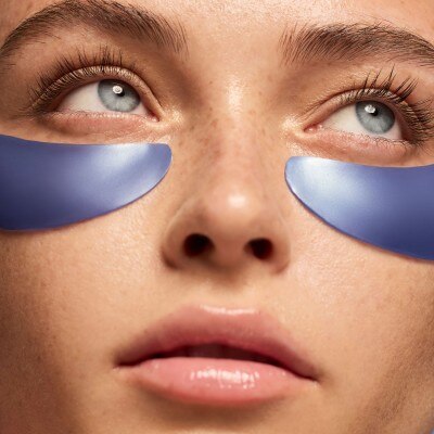 Close-up of a woman's face wearing blue under-eye patches beneath her eyes.
