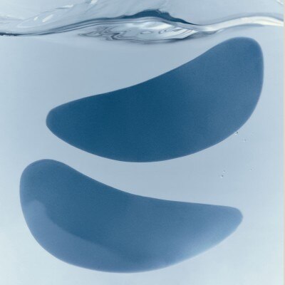 Two blue crescent-shaped silicone patches floating in clear water, with the water surface visible at the top.