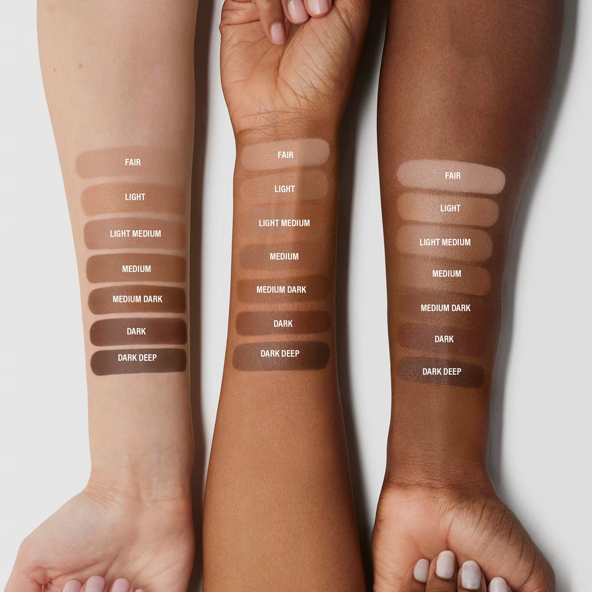 Three arms with different skin tones displaying a range of brown makeup swatches
