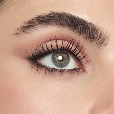 Close-up of a human eye with long, dark, curled eyelashes and a neatly shaped eyebrow on smooth skin.