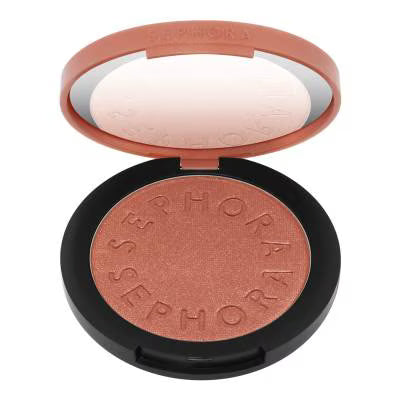 An open round makeup compact showing a shimmering rose gold pressed powder blush with the brand name 'SEPHORA' embossed around the edge. The compact has a black base and a peach-colored lid with a mirror, set against a plain white background.