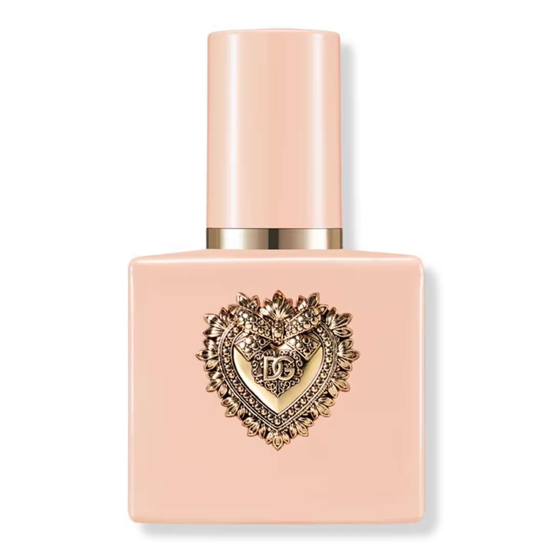 A square bottle of Dolce & Gabbana nail polish in a pale peach-pink shade, featuring a prominent gold heart-shaped logo with the brand initials 'DG' on the front, set against a plain white background.