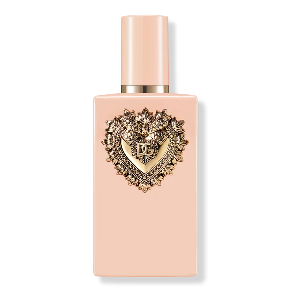 A pale peach rectangular perfume bottle with a matching cap and a prominent gold heart-shaped decorative emblem on the front, photographed on a clean white background.