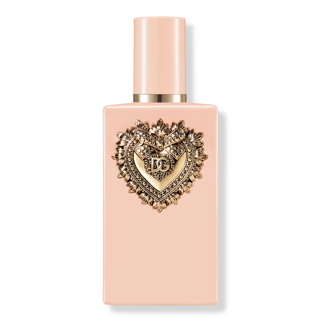 A pale peach rectangular perfume bottle with a matching cap and a prominent gold heart-shaped decorative emblem on the front, photographed on a clean white background.