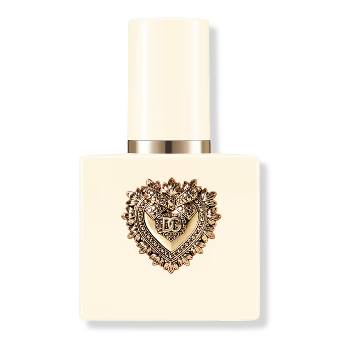 A square cream-colored perfume bottle with a matching cylindrical cap, featuring a prominent gold heart-shaped decorative emblem on the front with the letters 'DC' in the center, set against a plain white background.