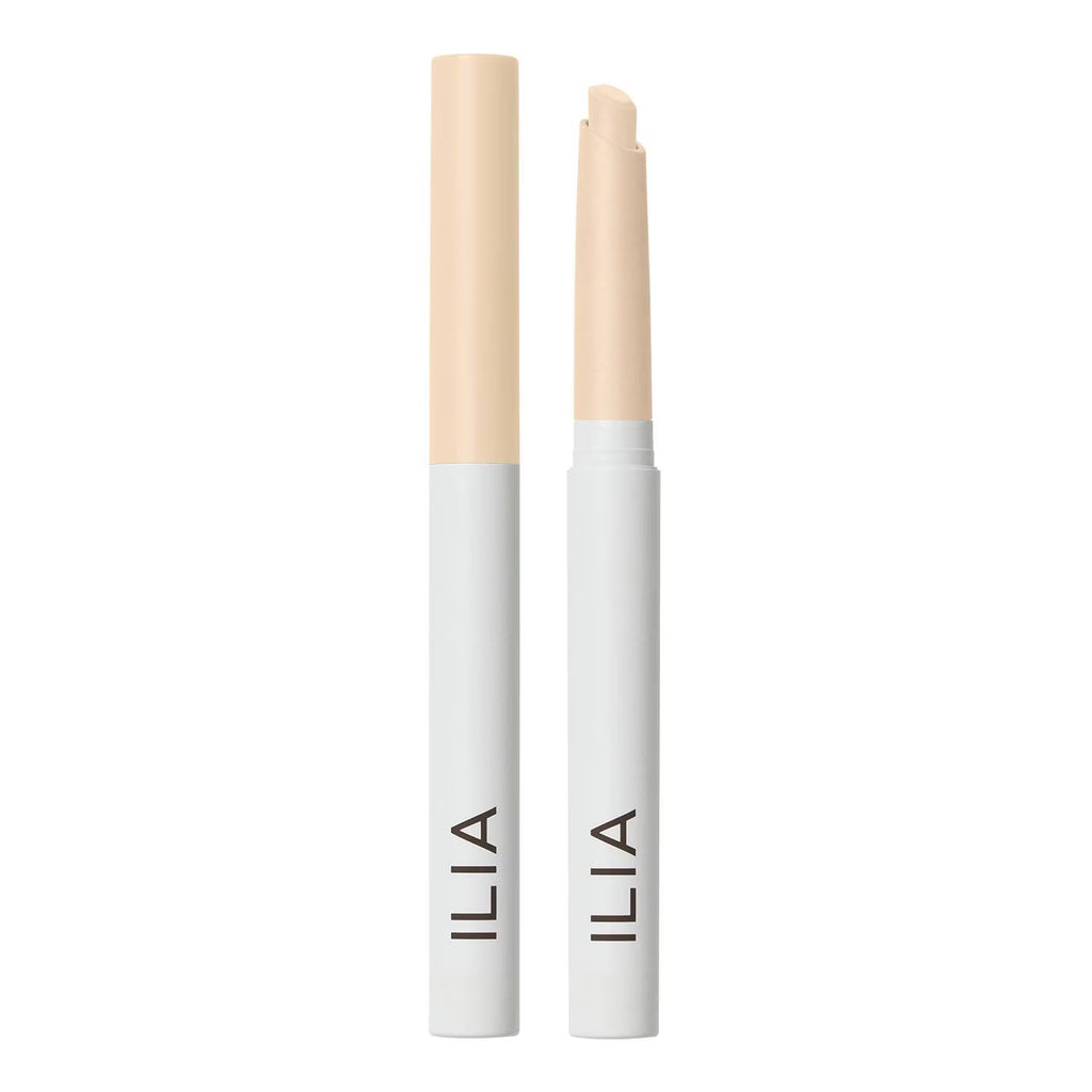 Two ILIA cosmetic sticks, one closed and one open, showing a light beige cream product in white and pale beige packaging on a solid white background.