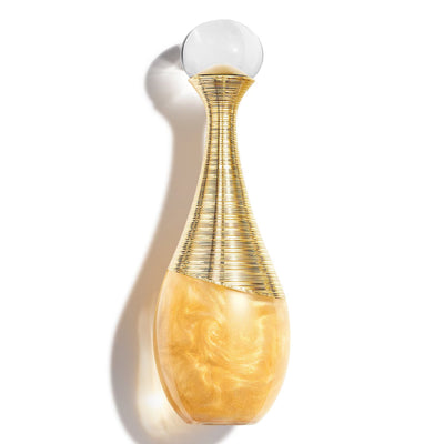 A Dior Addict perfume bottle with a textured gold neck, a marbled amber-yellow base, and a clear spherical cap, shown against a white background with a soft shadow.