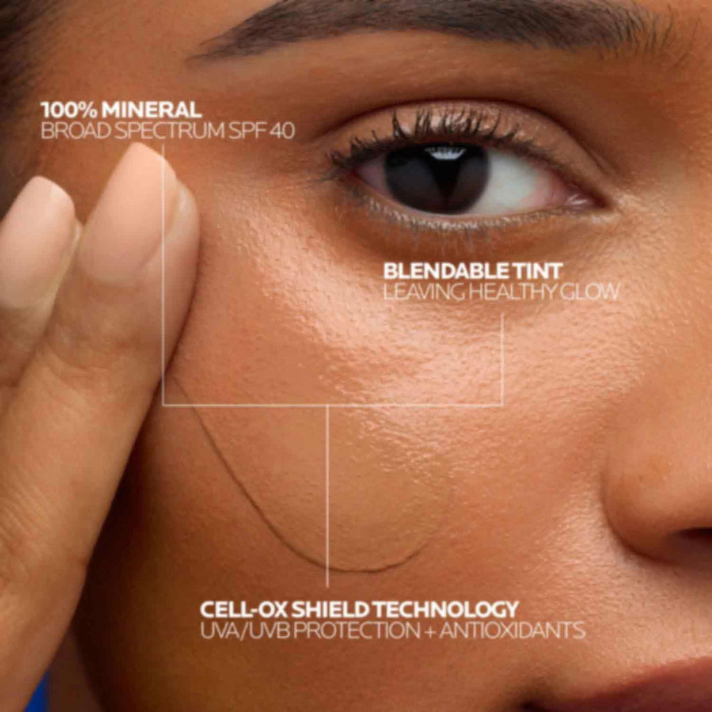 Close-up of a person's face highlighting a tinted sun protection cream patch on the cheek, with text overlays reading '100% MINERAL BROAD SPECTRUM SPF 40', 'BLENDABLE TINT LEAVING HEALTHY GLOW', and 'CELL-OX SHIELD TECHNOLOGY UVA/UVB PROTECTION + ANTIOXIDANTS'.