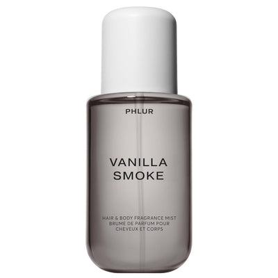 A bottle of PHLUR Vanilla Smoke Hair & Body Fragrance Mist, featuring a translucent smoky gray bottle and a matte white cap, set against a plain white background.
