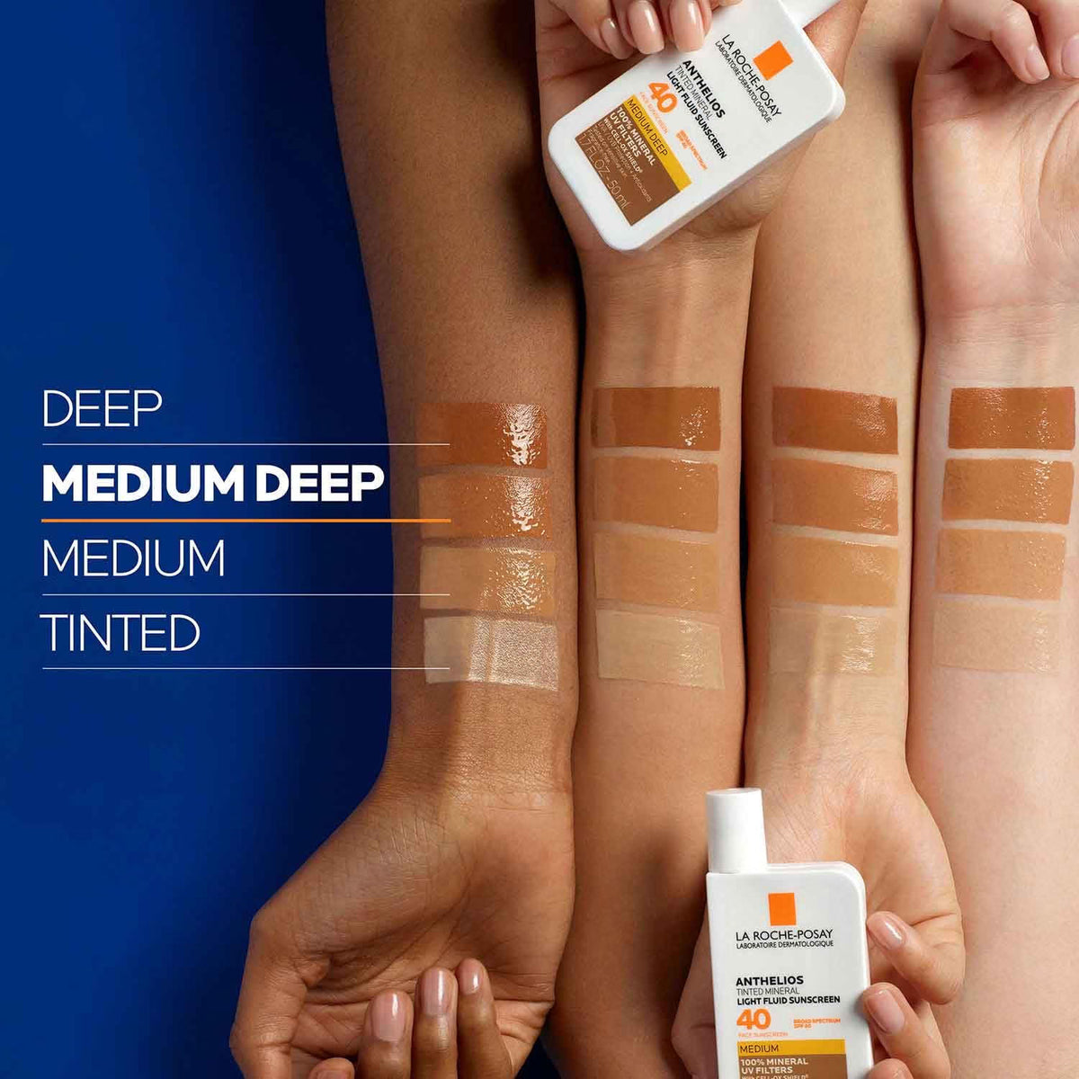 Hands holding bottles of sunscreen with color swatches on skin against a blue background