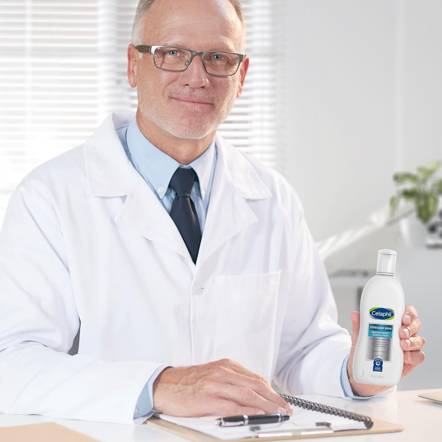A man in a white doctor's coat and glasses holds a bottle of Gelsomine hand sanitizer while sitting at a desk with a clipboard.