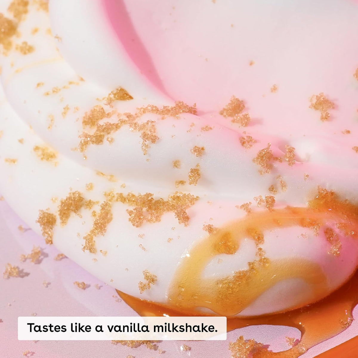 A close-up of a vanilla-flavored product with white and pink swirls, topped with brown sugar crystals and caramel drizzle, with the text 'Tastes like a vanilla milkshake.' overlaid at the bottom.
