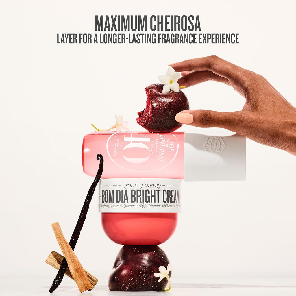 Bom Dia Bright Cream with a hand holding a red fruit, vanilla bean, and cinnamon stick on a white background.
