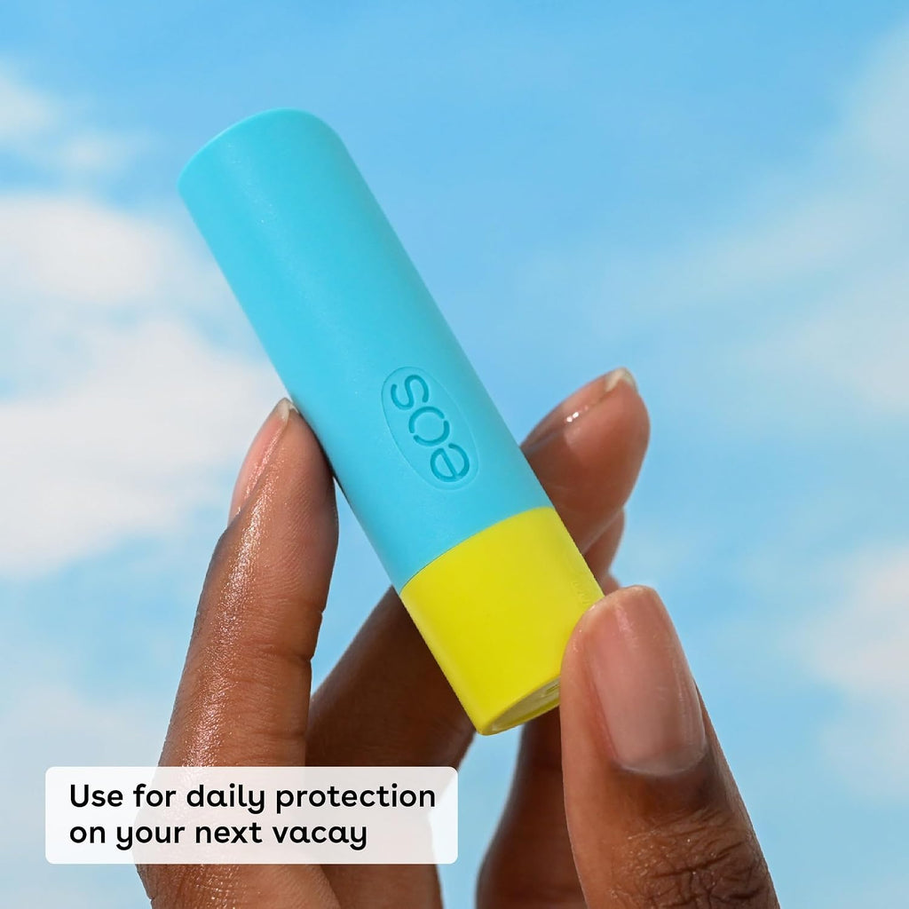Hand holding a blue and yellow lip balm with 'eos' branding against a blue sky.
