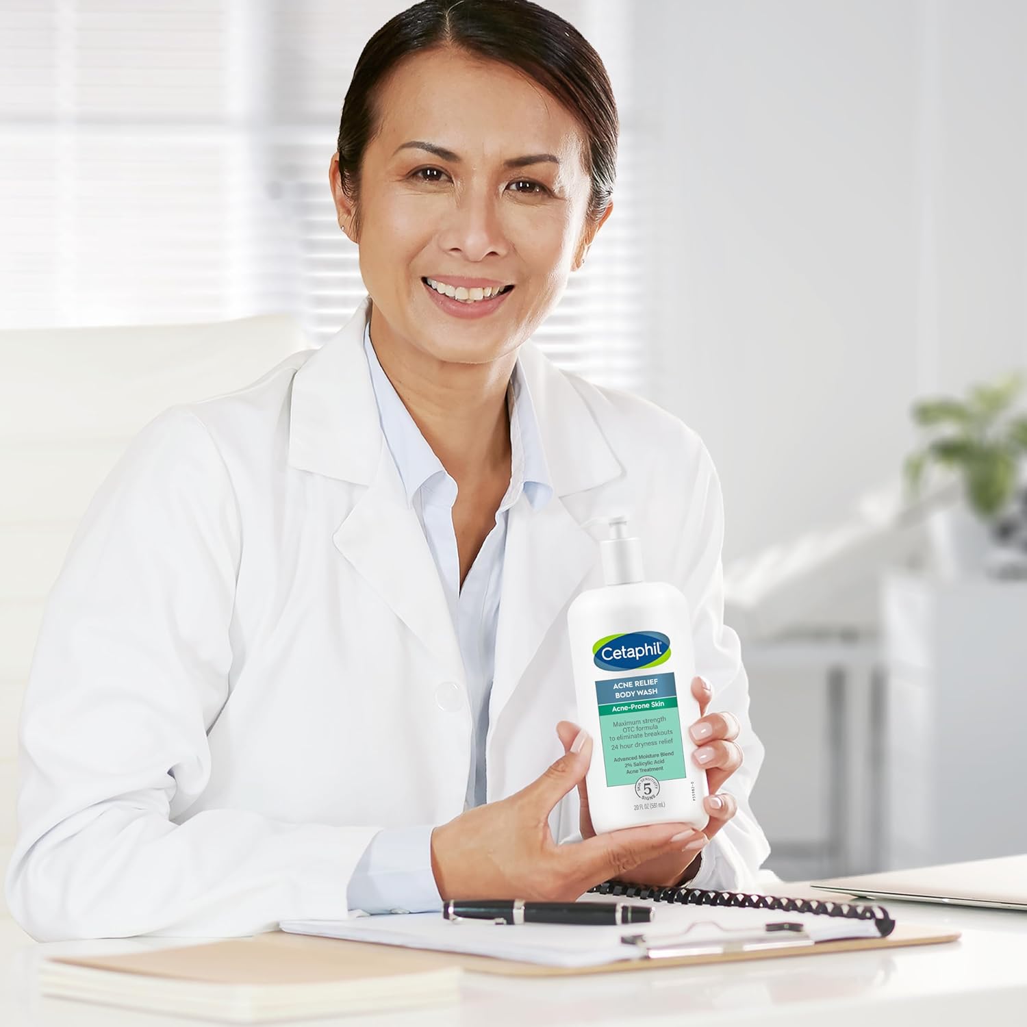 Person in a white coat holding a bottle of Cetaphil product in a clinical setting.