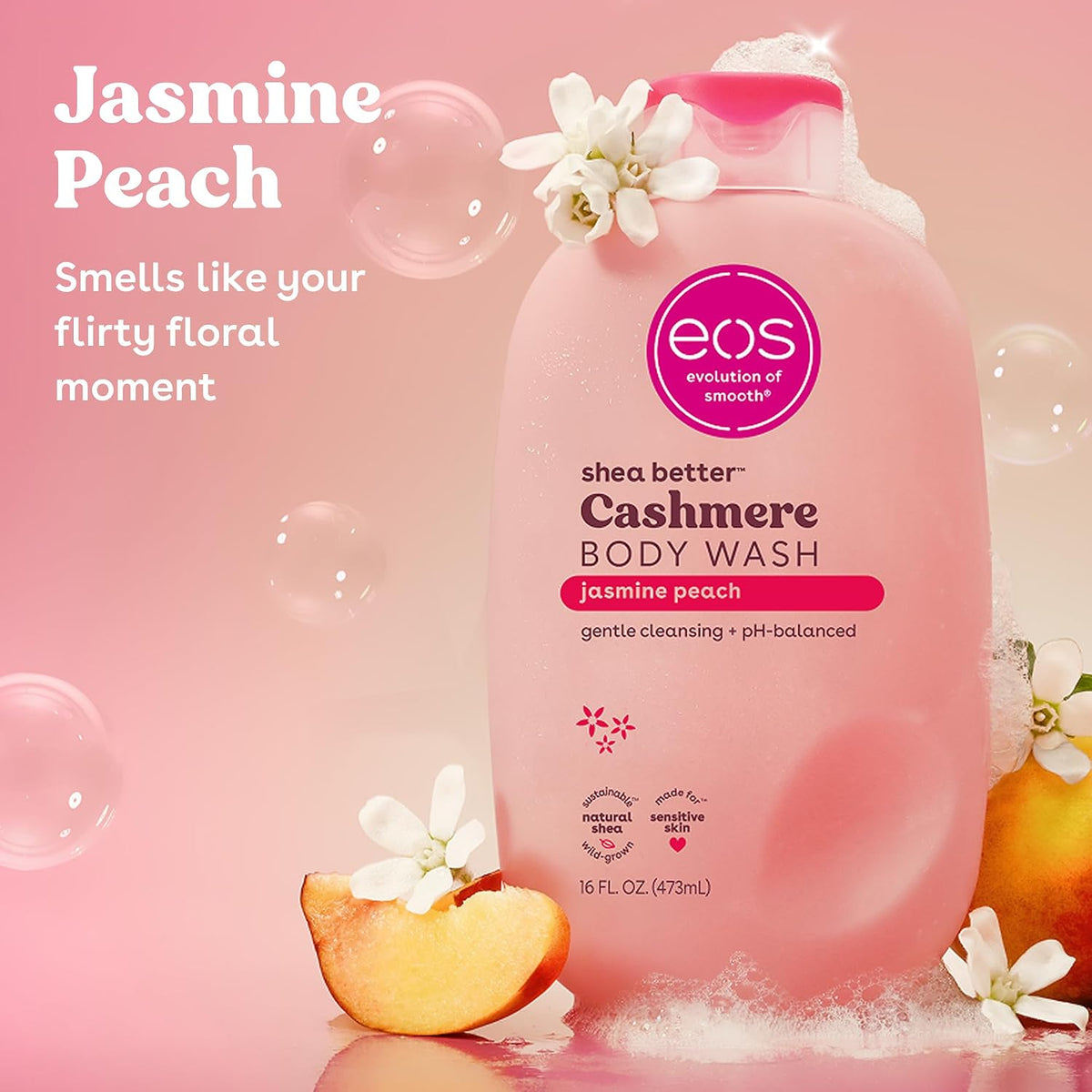EOS Cashmere Body Wash in Jasmine Peach scent, shown in a pink bottle with a pink cap, surrounded by decorative peach slices, white blossoms, and floating bubbles on a pink background.