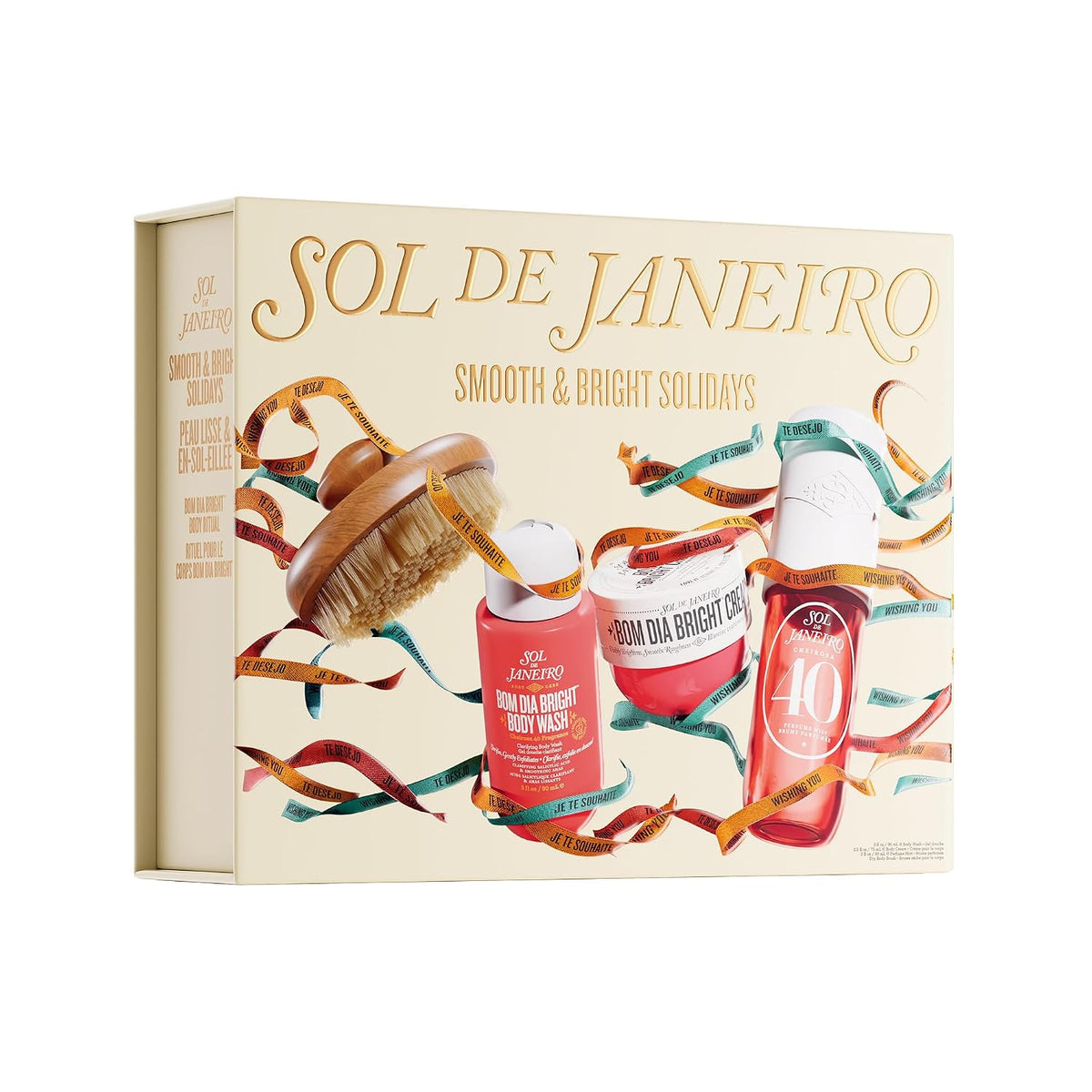 A gift set box held by two hands, featuring the brand name 'SOL DE JANEIRO' and holiday-themed illustrations of body care products and festive ribbons. Text at the top reads 'FEATURING MIDI SIZES OF PERFUME MIST (90 ML) & BODY CREAM (75 ML), PLUS A BODY BRUSH'.