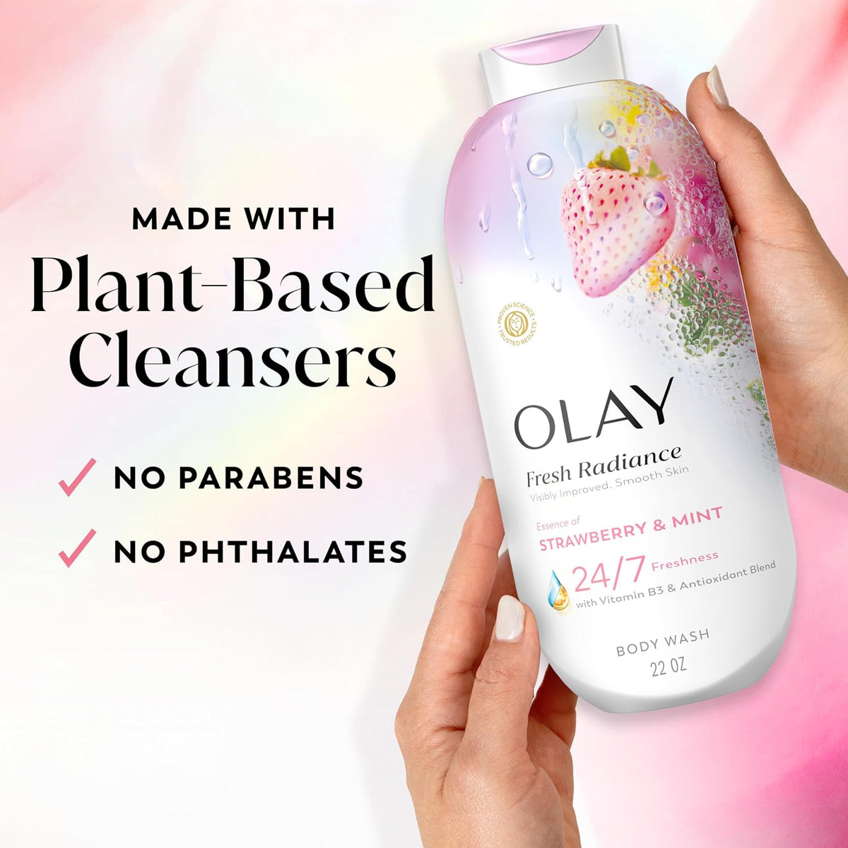 A hand holds an Olay Fresh Radiance Strawberry & Mint body wash bottle against a soft pink and white background with marketing text about plant-based cleansers and no parabens/phtalates.