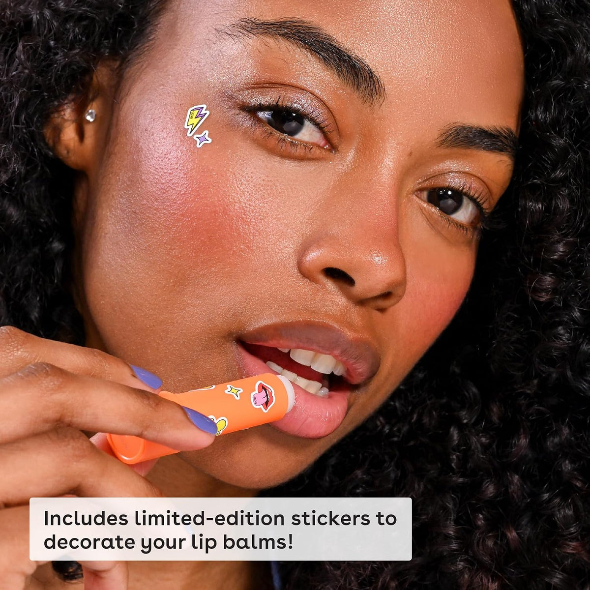 Woman holding an orange lip balm with limited-edition stickers, close-up of face.