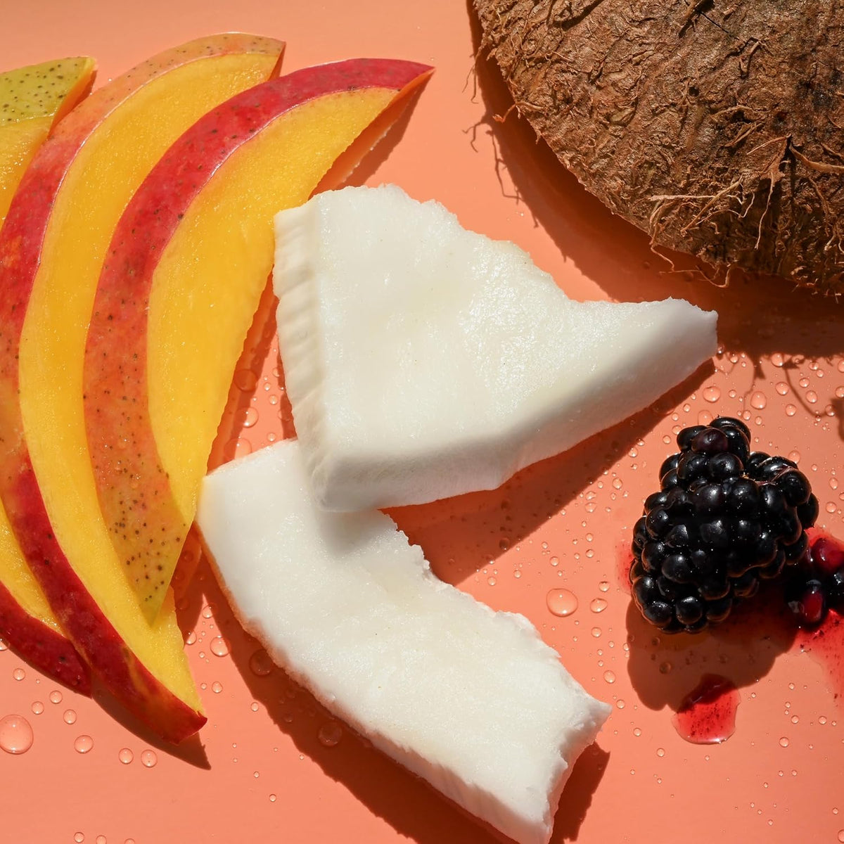 Fruit slices including mango, coconut, and blackberries on a pink background