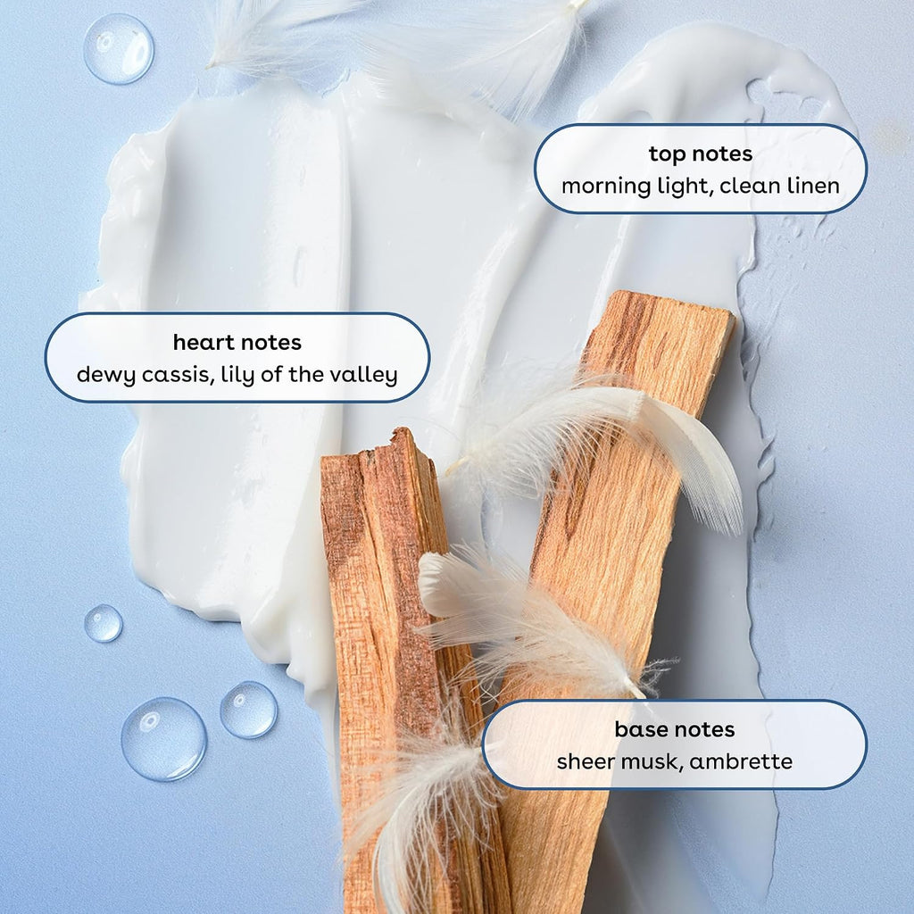 A styled fragrance note graphic on a pale blue background with white cream, feather strands, and two wood chips. Text labels identify top notes as 'morning light, clean linen,' heart notes as 'dewy cassis, lily of the valley,' and base notes as 'sheer musk, ambrette.