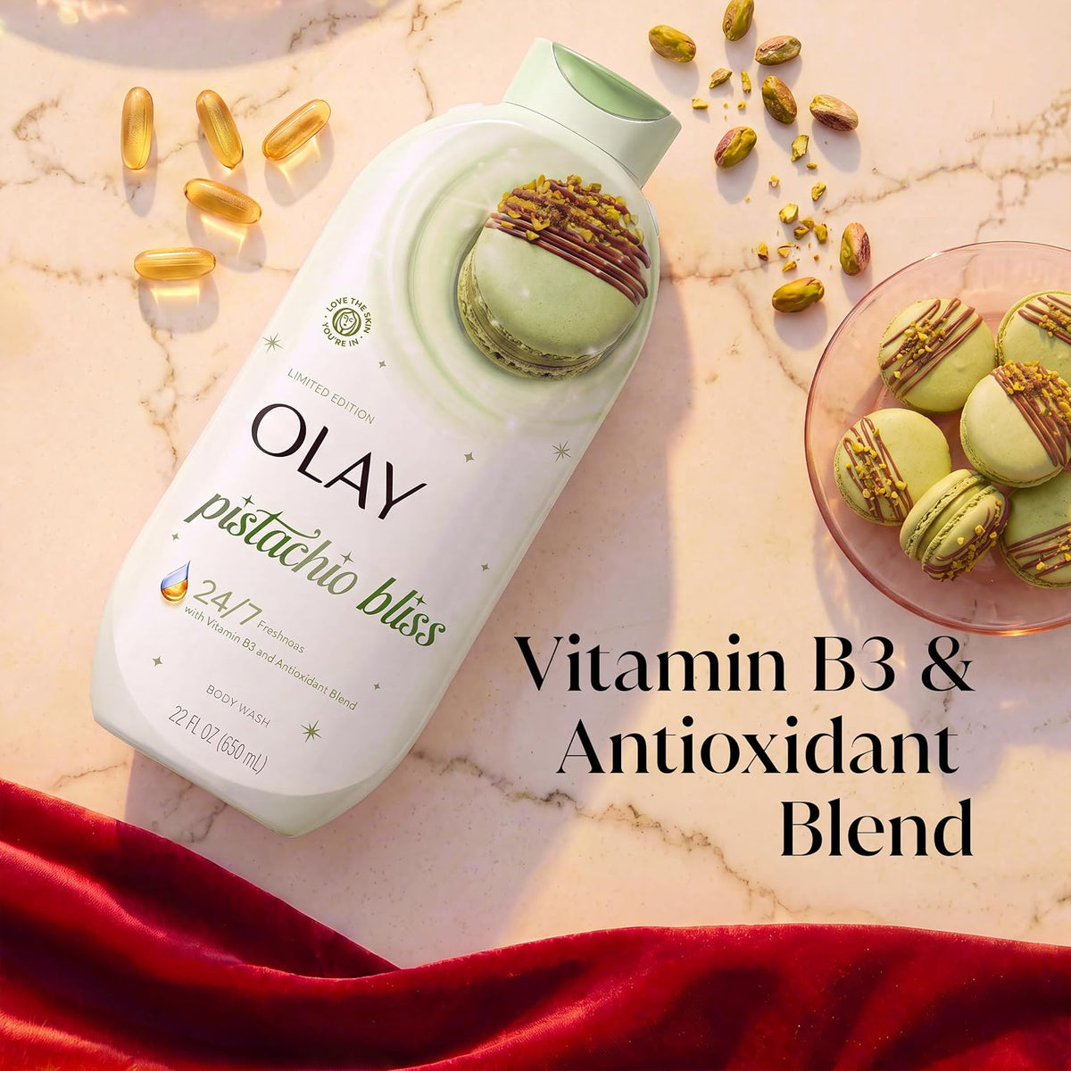 Olay Pistachio Bliss Vitamin B3 & Antioxidant Blend face wash bottle on a marble surface, styled with pistachios, macarons, and gold capsules, with a red velvet cloth at the bottom.
