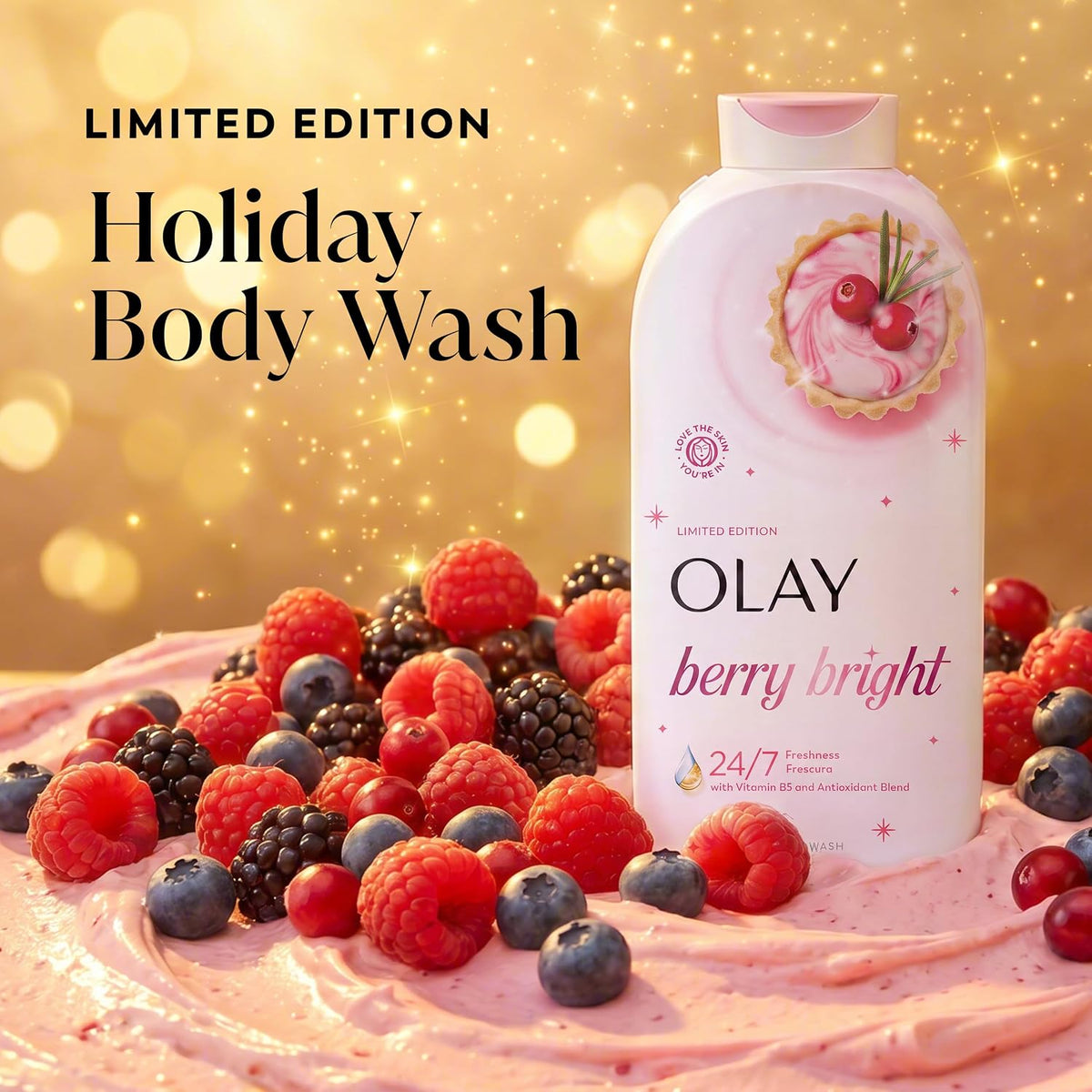 Olay Holiday Body Wash Limited Edition bottle in Berry Bright scent, styled on a pink whipped cream surface with fresh raspberries, blueberries, and blackberries against a sparkling gold bokeh background.