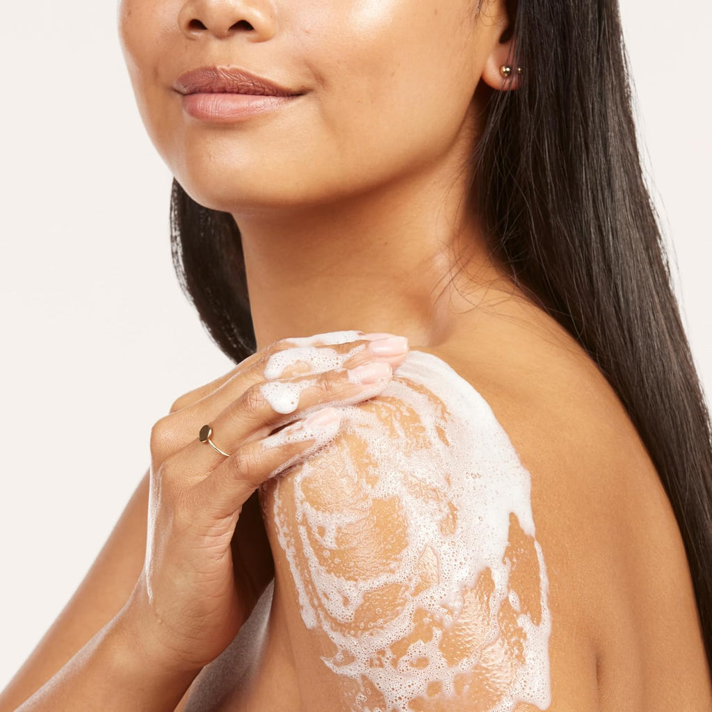 Woman applying a white cream or lotion to her shoulder against a neutral background
