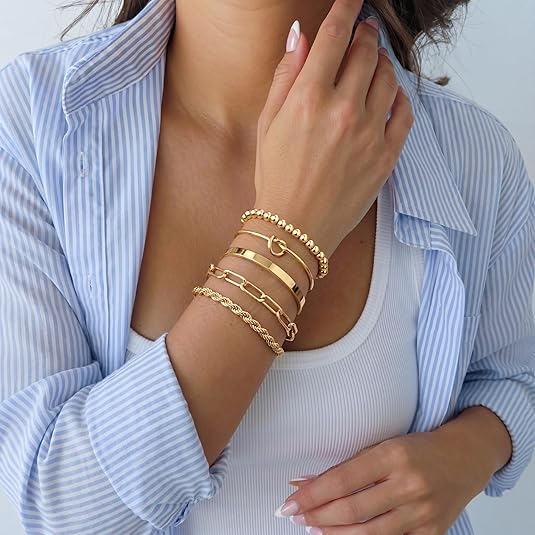 Woman wearing multiple gold bracelets on her wrist with a light blue striped shirt.