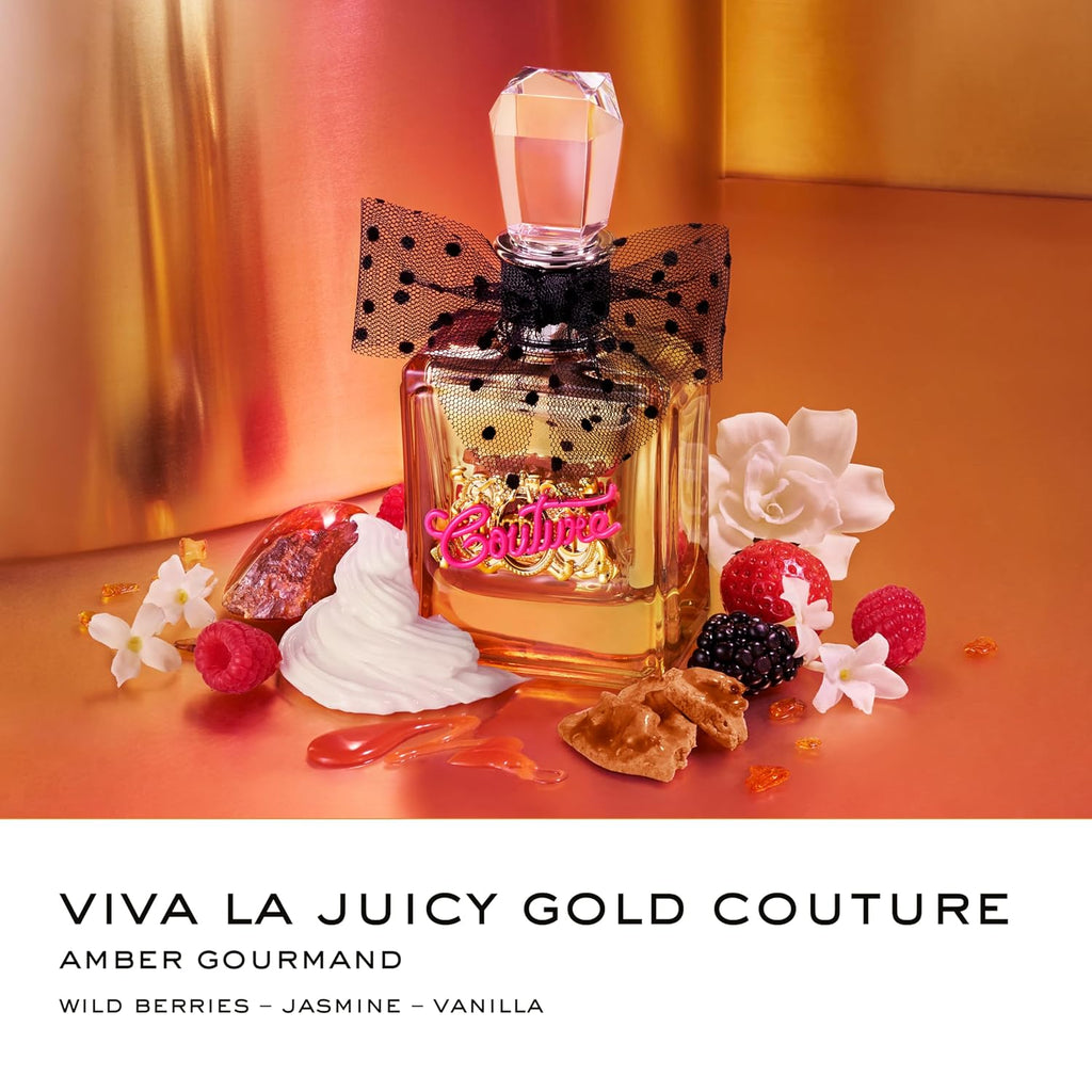 Viva La Juicy Gold Couture Amber Gourmand perfume bottle with a black polka dot bow, surrounded by fresh berries, white flowers, and pastry pieces on a warm amber background. The bottom of the image features a white banner with the text 'VIVA LA JUICY GOLD COUTURE AMBER GOURMAND' and 'WILD BERRIES - JASMINE - VANILLA'.