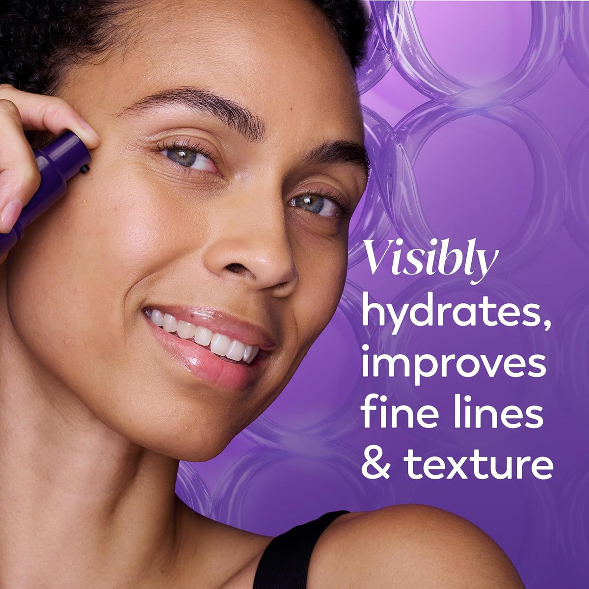 A smiling woman with short dark hair applies a purple skincare product to her cheek against a purple background with text that reads, 'Visibly hydrates, improves fine lines & texture.'.