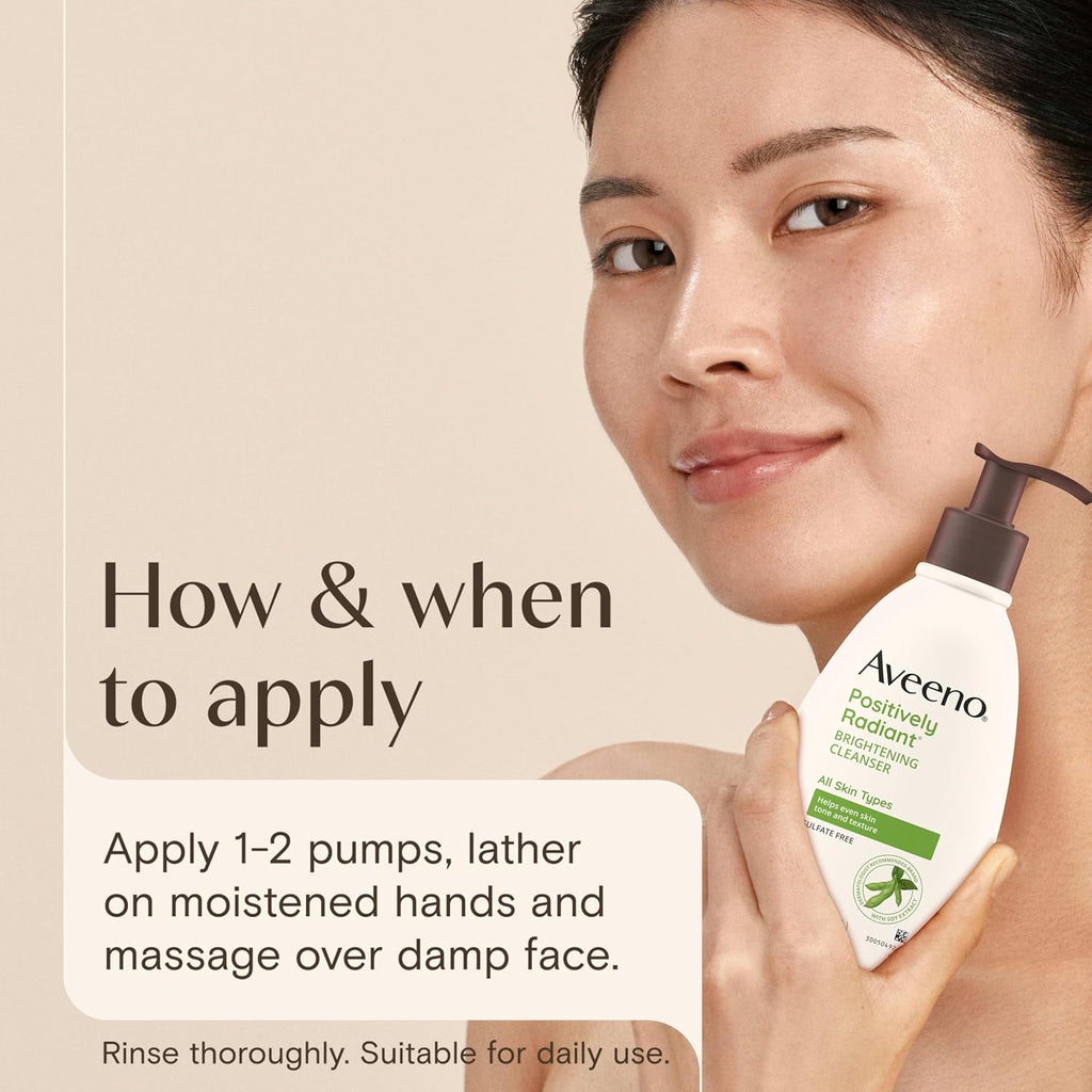 A woman holds an Aveeno Positively Radiant Smoothing Emulsion bottle against a warm beige background with text explaining how to apply the product.