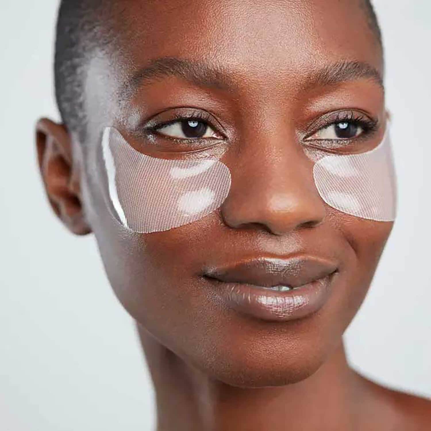 Woman wearing under-eye patches on a plain background