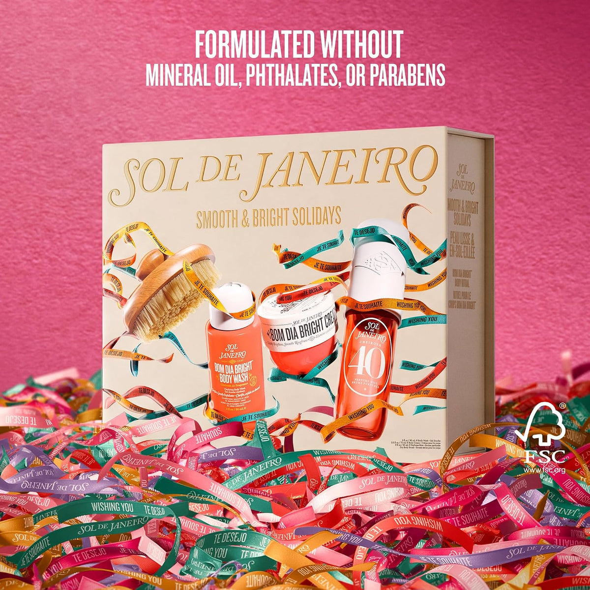 A gift set box held by two hands, featuring the brand name 'SOL DE JANEIRO' and holiday-themed illustrations of body care products and festive ribbons. Text at the top reads 'FEATURING MIDI SIZES OF PERFUME MIST (90 ML) & BODY CREAM (75 ML), PLUS A BODY BRUSH'.