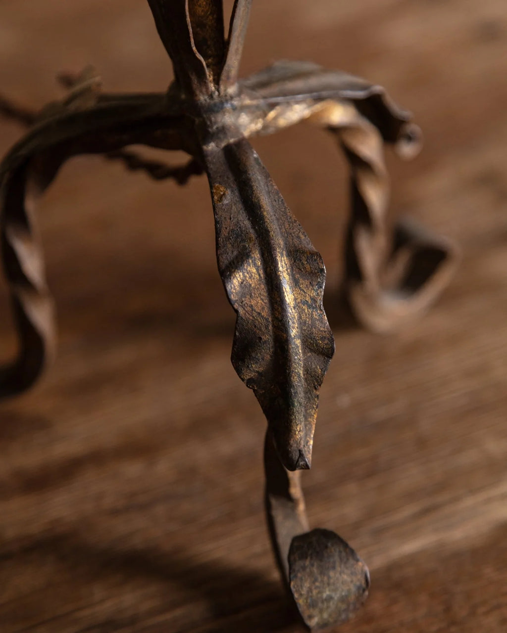 Close-up of a dark metal stand or frame with leaf-like curled arms, photographed on a wooden surface.
