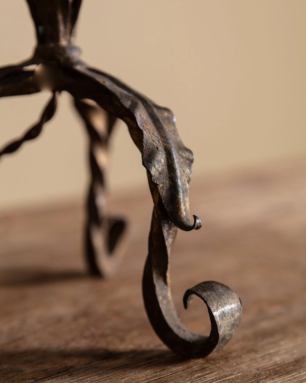 Close-up of a dark wrought iron scrollwork stand or frame leg resting on a wooden surface against a warm beige background.
