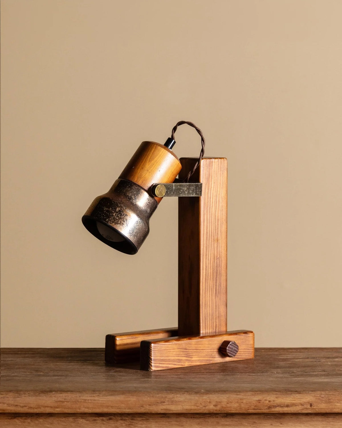 A rustic industrial-style table lamp with a wooden and metal body, shown on a wooden tabletop against a solid beige background.