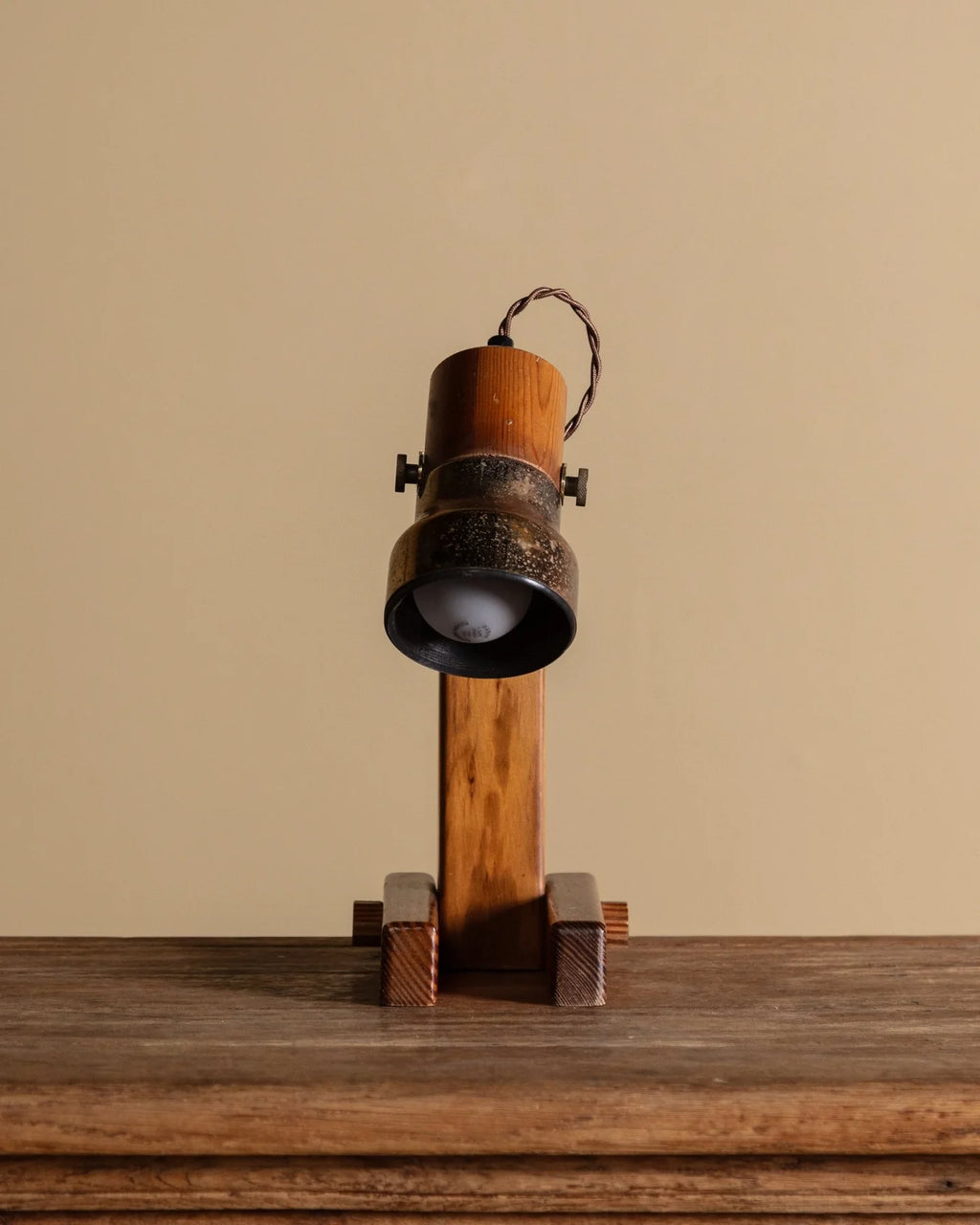 A vintage-style table lamp with a cylindrical wooden shade, a dark metal band, and a wooden stand, set against a solid beige background.