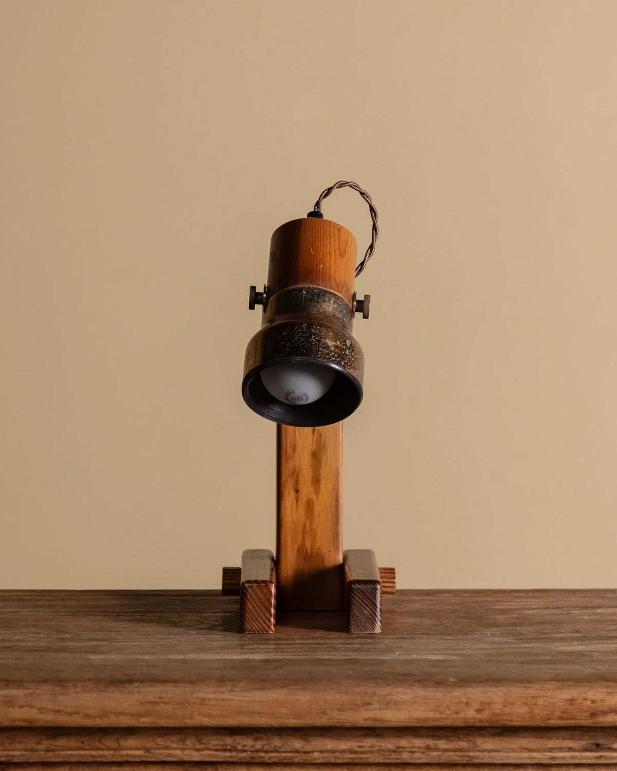 A vintage-style table lamp with a cylindrical wooden shade, a dark metal band, and a wooden stand, set against a solid beige background.