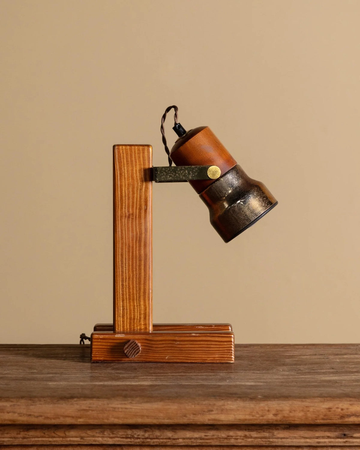 A vintage-style adjustable table lamp with a wooden base and arm, a brown leather shade, and a dark metal lamp head, shown on a wooden surface against a beige background.