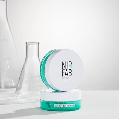 NIP+FAB Hydroxite Extreme Jelly Eyetree jar in a white and teal color scheme, styled with clear glass laboratory flasks in the background on a white surface.