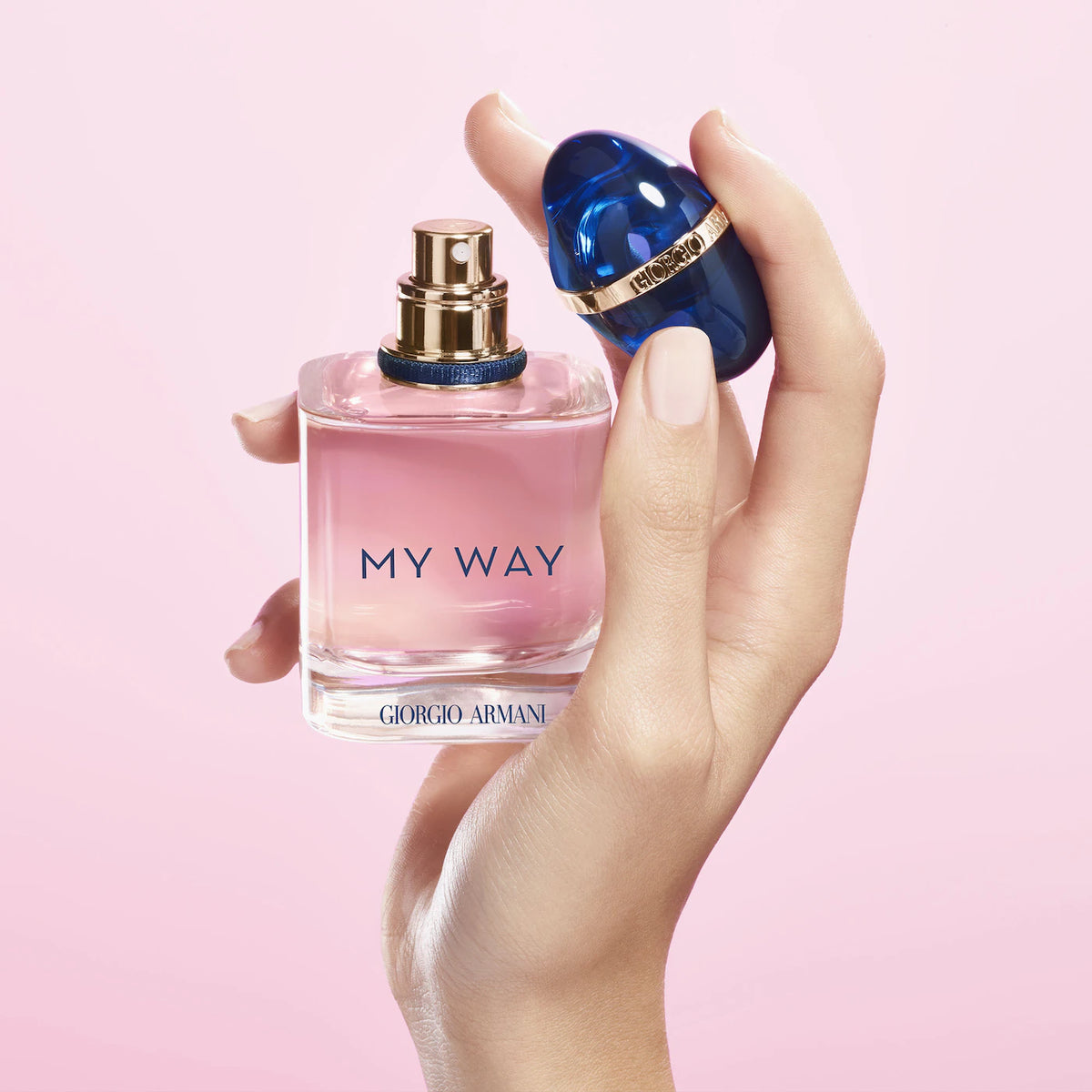 Hand holding a pink 'My Way' Giorgio Armani perfume bottle against a light pink background