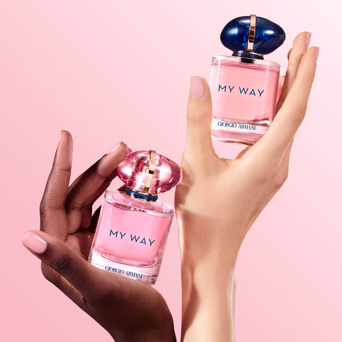 Two hands holding Giorgio Armani 'My Way' perfume bottles against a pink background