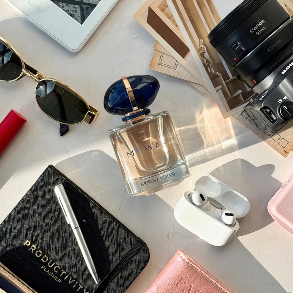 Perfume bottle, sunglasses, camera, and other items on a light surface