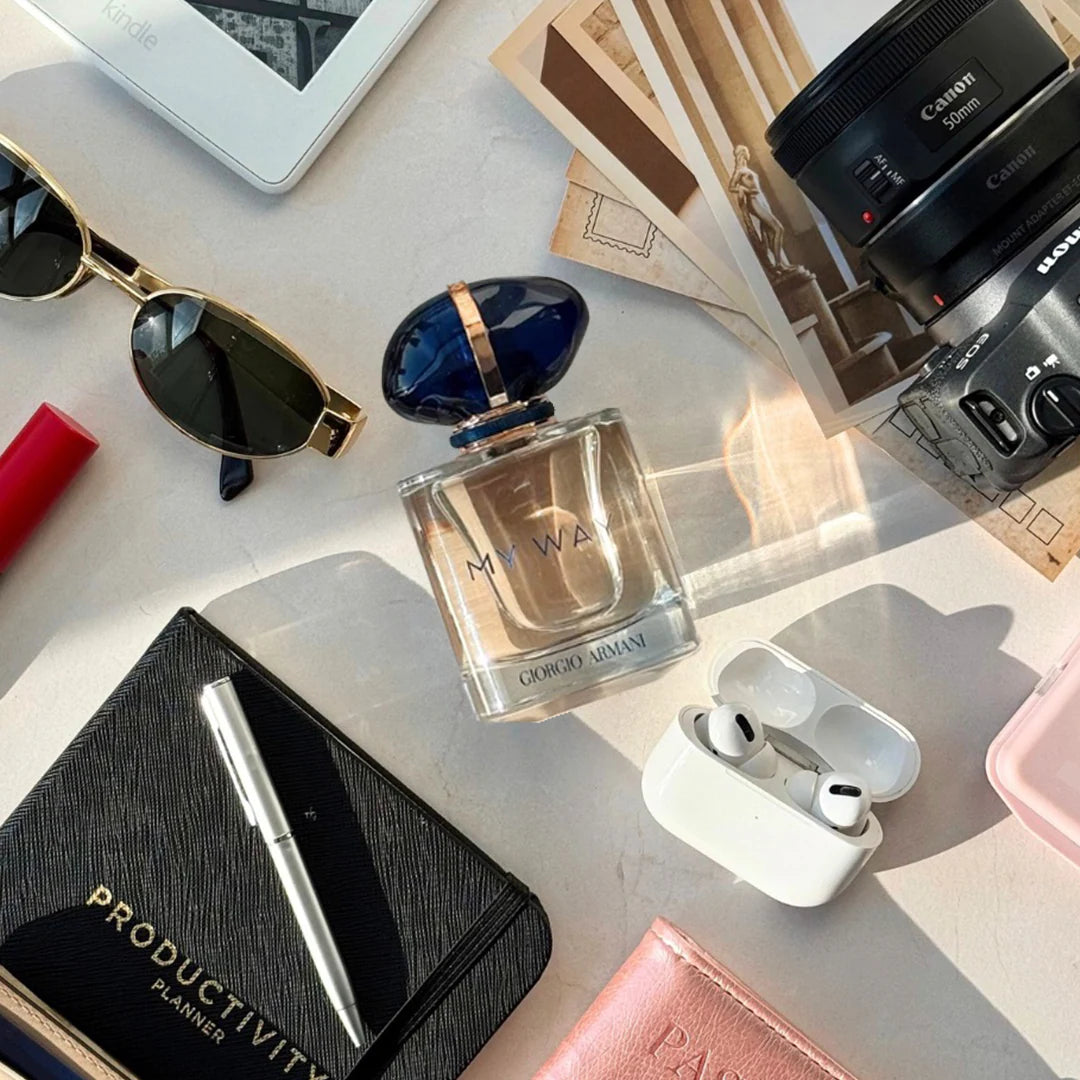 Perfume bottle, sunglasses, camera, and other items on a light surface