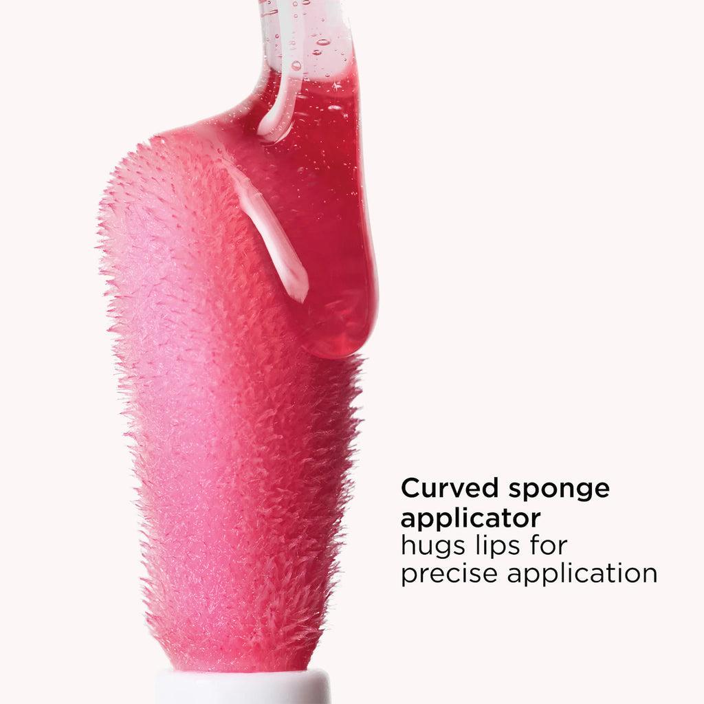 Close-up of a pink textured curved sponge applicator with glossy pink product on the tip, shown against a very light neutral background with the text 'Curved sponge applicator hugs lips for precise application'.
