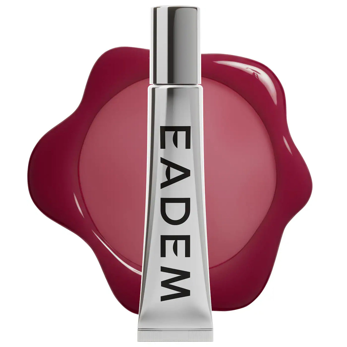 A silver tube of EADEM lip gloss with black lettering, set against a glossy deep pink wax seal shape on a white background.