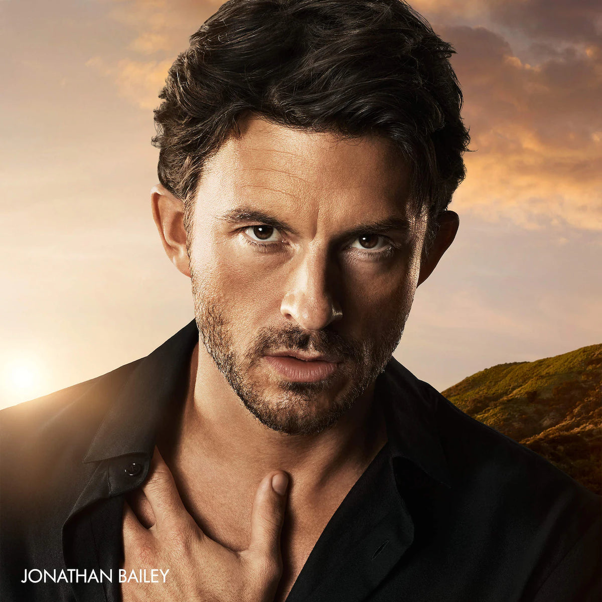 Jonathan Bailey in a black shirt against a warm sunset sky with hills in the background, with the text 'JONATHAN BAILEY' in the lower left corner.