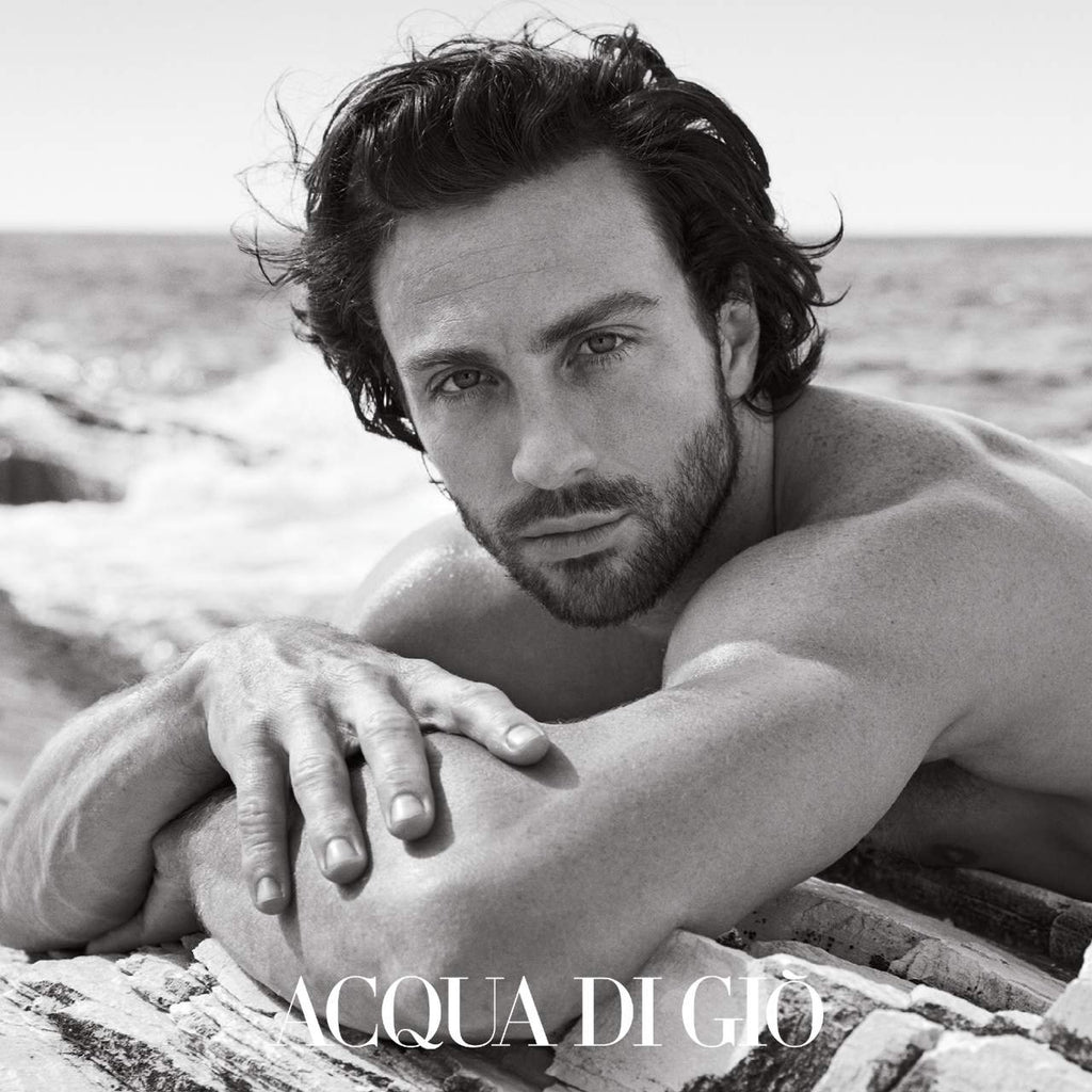 Man lying on a log by the water with 'Acqua di Gio' branding.